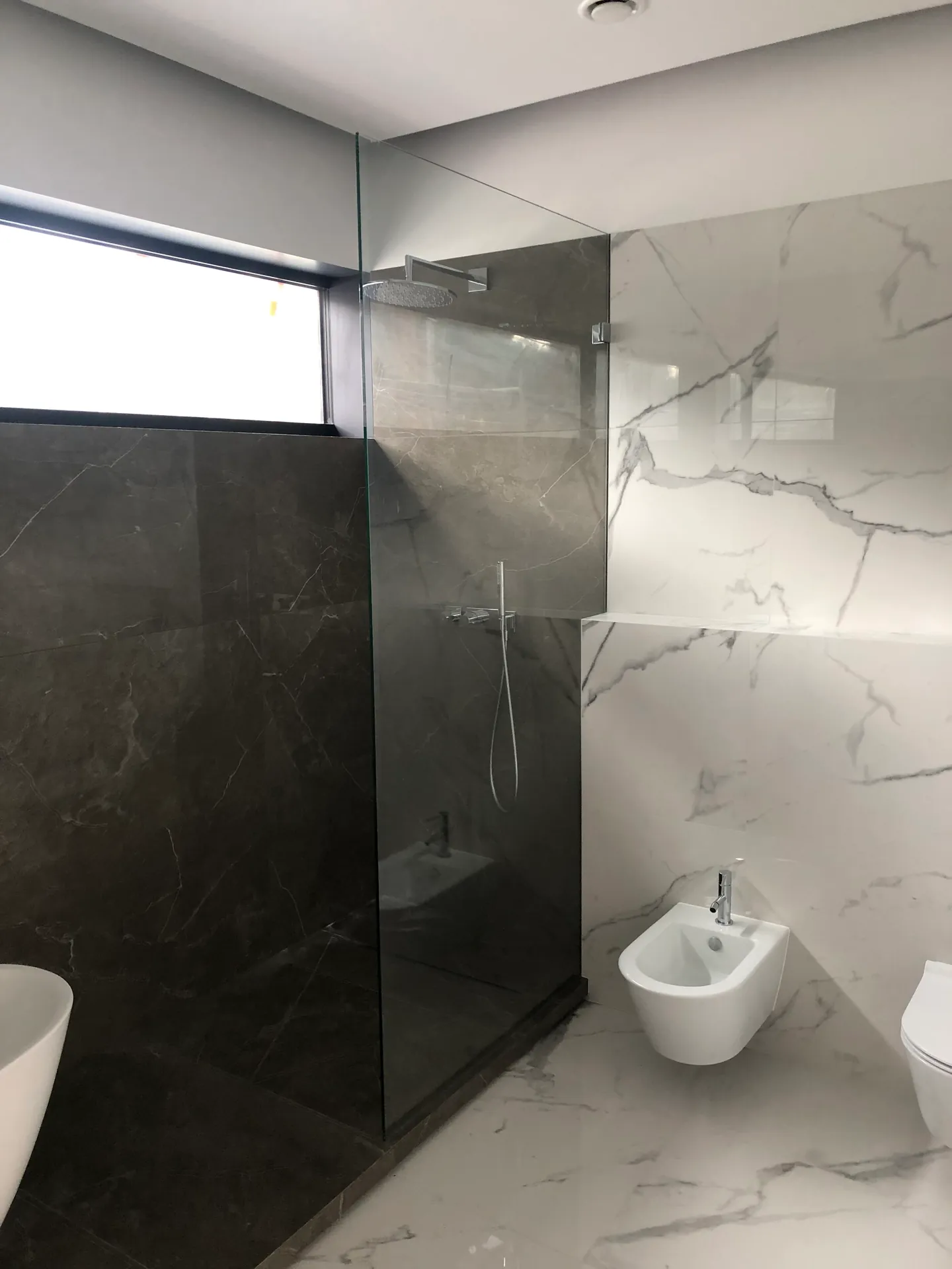 Bezramowa szyba walk-in pod podłużnym oknem w marmurowej łazience