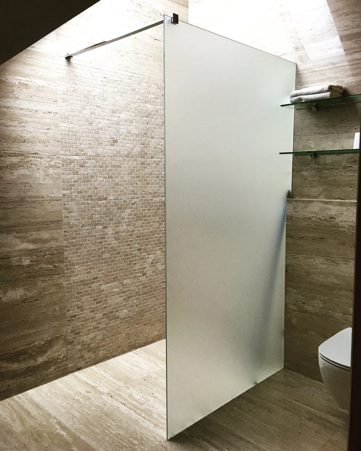 Matowa szyba walk-in z chromowanym wspornikiem w kamiennej łazience