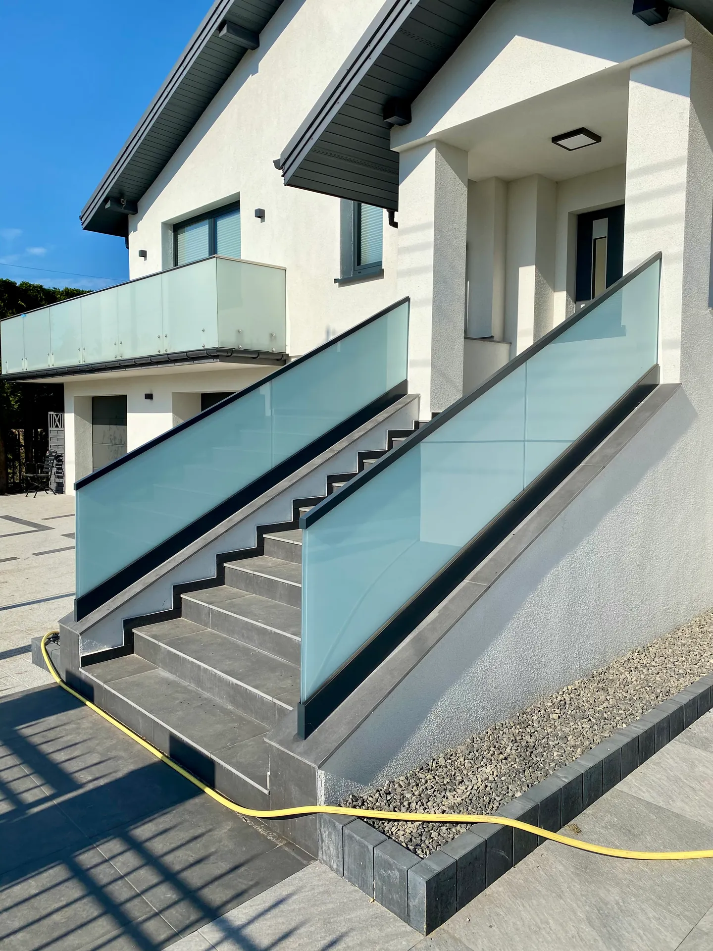 Matowe balustrady szklane przy schodach wejściowych i balkonie domu