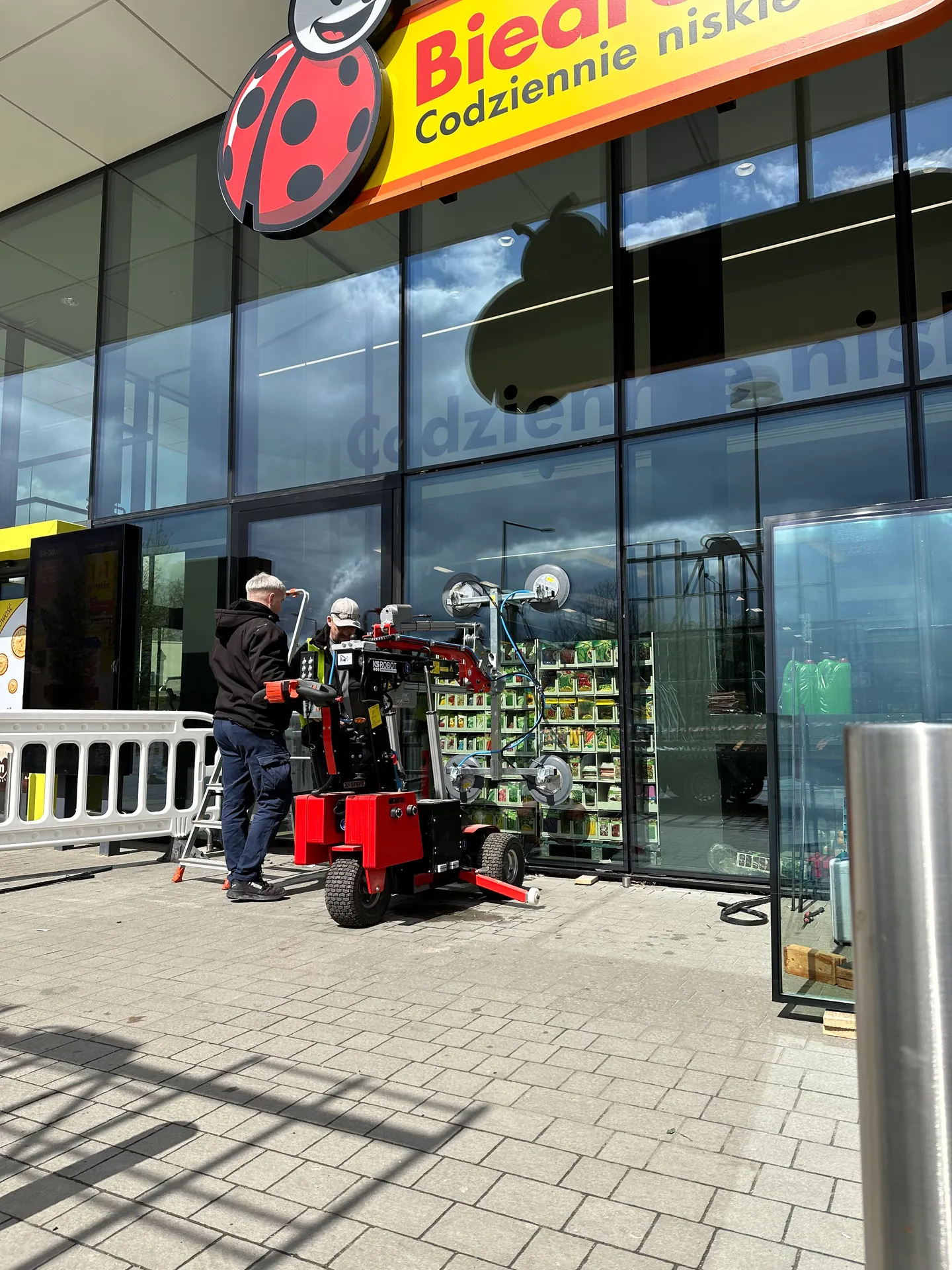 Montaż dużej szyby witrynowej robotem przy wejściu do sklepu Biedronka