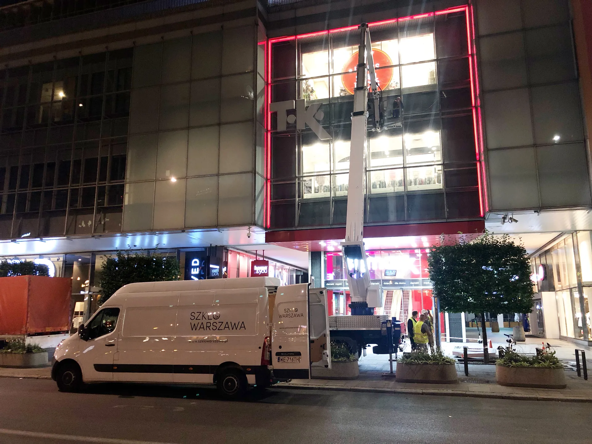 Nocne prace z podnośnika przy przeszklonej fasadzie centrum handlowego